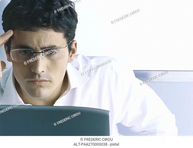 Businessman wearing glasses, furrowing brow, looking at computer screen