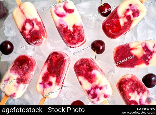 Fresh, homemade, delicious, cherry and milk ice cream popsicles placed on glass tray filled with ice cubes. Top view, flat lay
