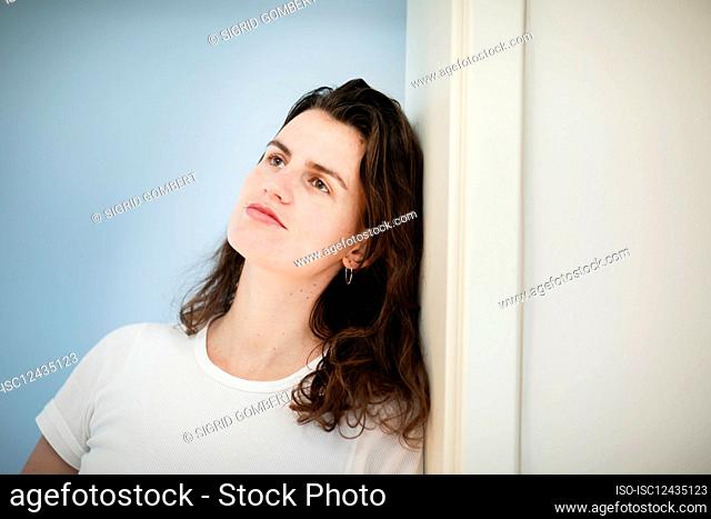 Pensive woman leaning against wall at home