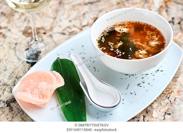 Crab soup served in white ceramic bowl with spoon, green leaf. pink crab chips and glass of white wine