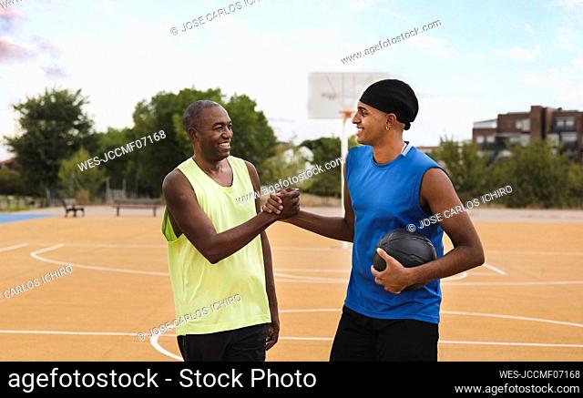 Smiling father and son doing handshake at sports court