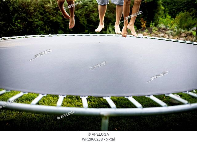 Low section of people jumping on trampoline at yard