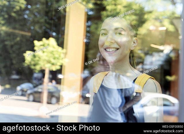 Smiling non-binary person seen through glass