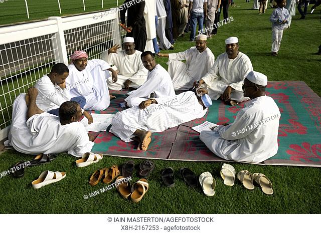 Muslim men checking horse form and placing bets at horse racing meeting at Al Meydan racecourse at night in Dubai United Arab Emirates