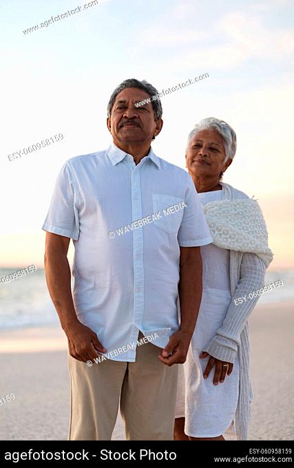 Biracial senior man and woman looking away at beach against sky during sunset