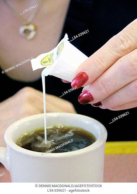 Woman pours cream in a cup of coffee