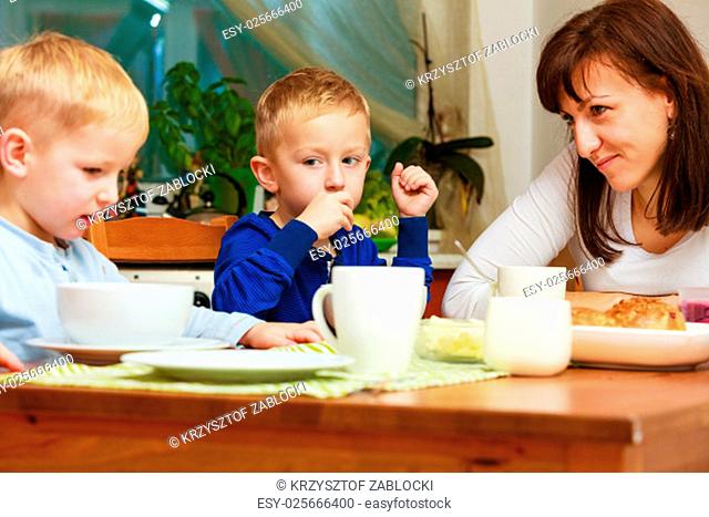 happy family. mother and sons boys kids children eating corn flakes and bread breakfast morning meal together at the table. home