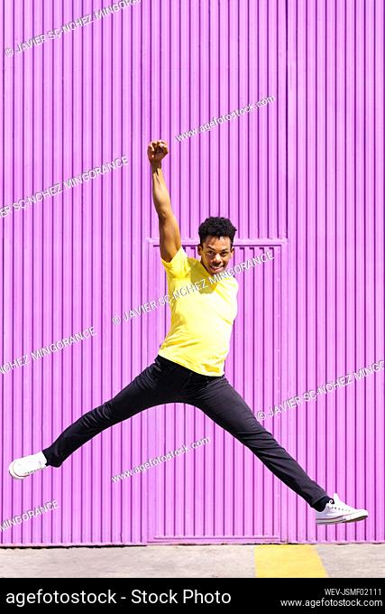 Smiling mid adult man with arms raised jumping on footpath