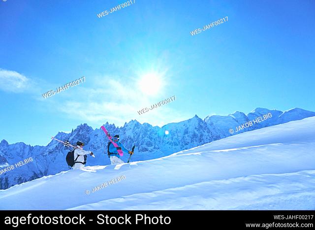 Woman and man carrying skies and walking on snowcapped mountain