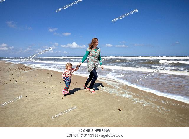 England, Norfolk, Horsey. A mother and daughter running along the beach at Horsey on the Norfolk coast