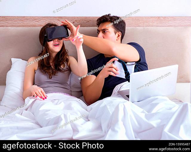 The wife and husband with virtual reality goggles in the bed