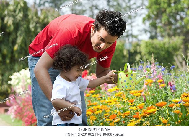 Boy watering plants with his father in a garden