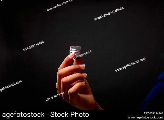 Close up of hand holding bulb screw base against black background