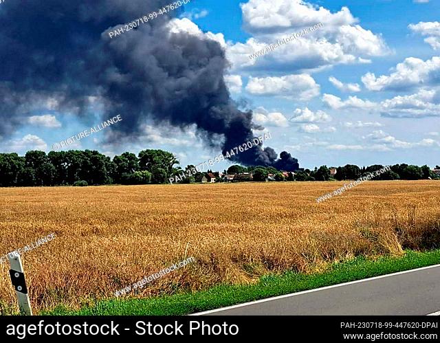 18 July 2023, Brandenburg, Brück: A black column of smoke rises into the sky above Brück in the district of Potsdam-Mittelmark during a fire (shot through the...