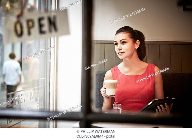 Young woman sitting in cafe with digital tablet and hot drink