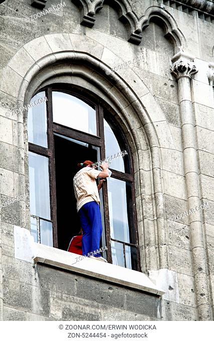 Eine Frau putzt Fenster und steht dabei gefährlich auf dem Fenstersims