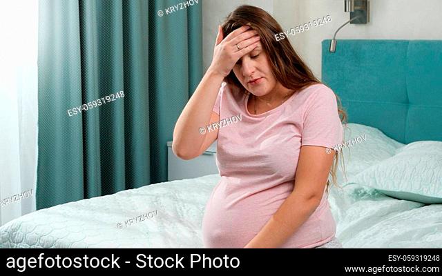 Portrait of upset pregnant woman feeling lonely and upset sitting on bed at home. Concept of maternal and pregnancy depression