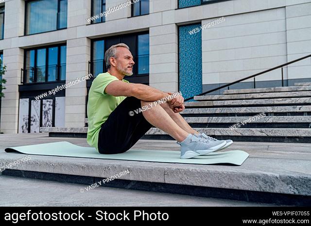 Thoughtful man sitting on yoga mat by steps