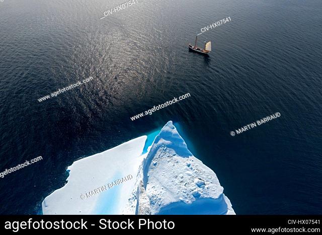 Drone point of view ship sailing past iceberg on sunny ocean Greenland
