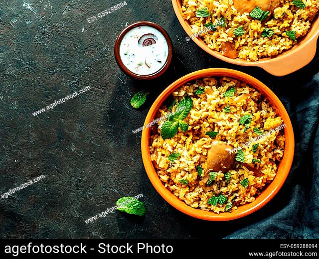 Pakistani food - biryani rice with chicken and raita yoghurt dip. Delicious hyberabadi chicken biryani in two bowl over black background