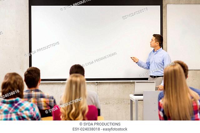 education, high school, technology and people concept - teacher standing with remote control, laptop computer in front of white board and students in classroom
