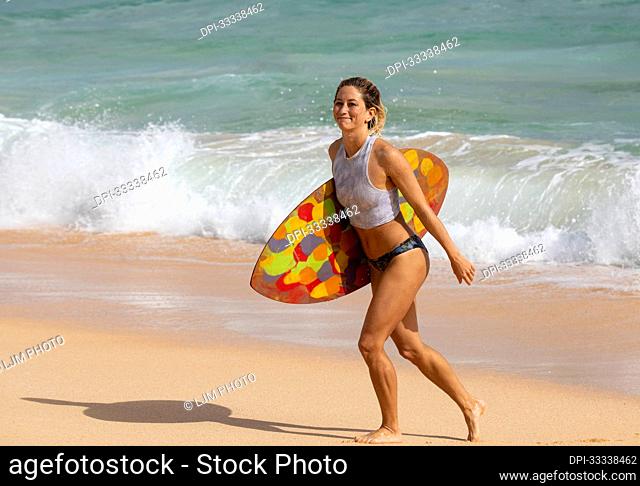 A beautiful young woman who is a professional skimboarder having fun at Sandy Beach; Oahu, Hawaii, United States of America