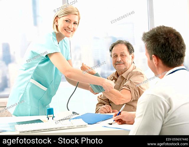 Old patient at examination in doctor's office, smiling nurse measuring blood pressure
