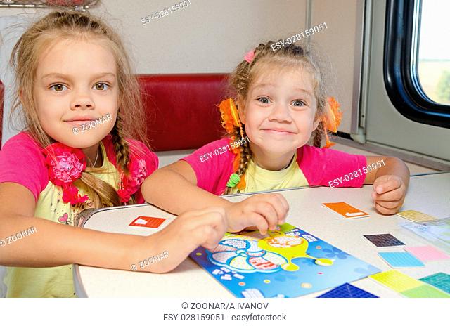 Two little sisters in the train of fun playing at the table at the lower place in the second-class compartment wagon