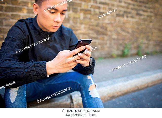 Young man sitting outdoors, using smartphone