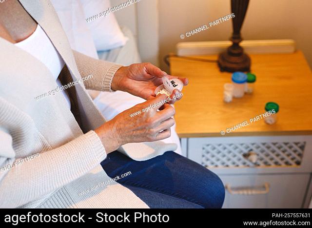Mid section of senior caucasian woman in bedroom sitting on bed, holding pills. retirement lifestyle, illness and the aging process || Model approval available