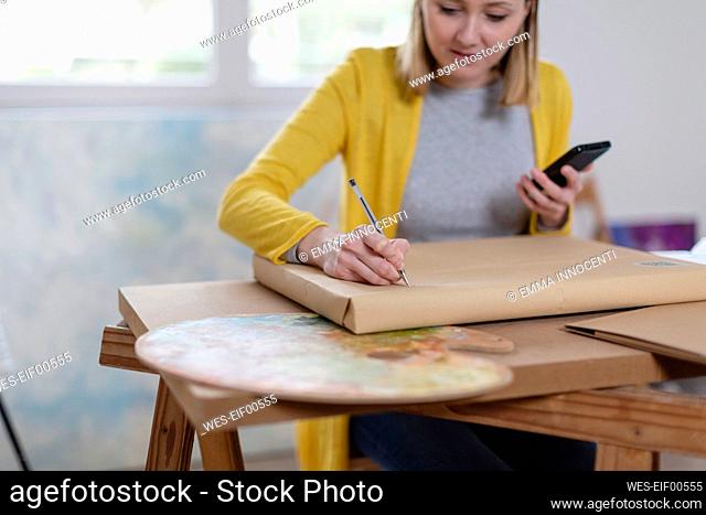 Female painter writing on delivery package at home studio
