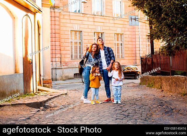 The tourist family of four people goes up the street of the old town. The man, the woman and two little girls walk around a European city
