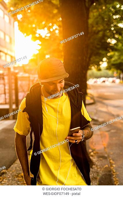 Smiling young man at backlight looking at cell phone