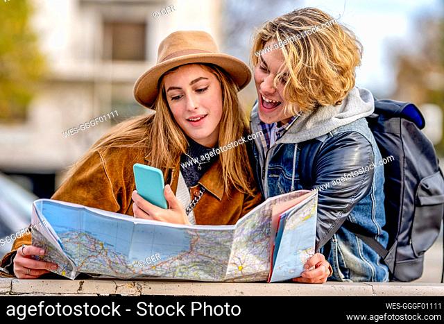 Man sharing smart phone with woman holding map on vacation