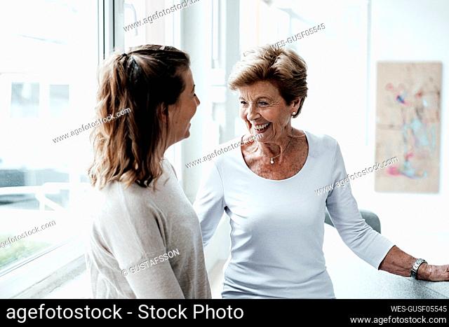 Cheerful grandmother smiling at young woman at home