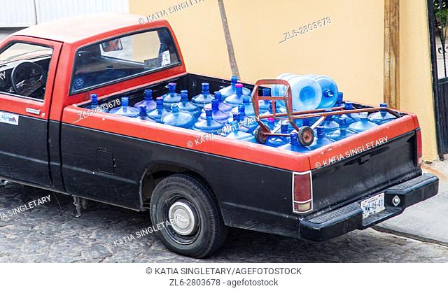 A red and black beat-up pick-up truck filled with blue huge water bottles refills ready to be delivered. In Cabos San Lucas, Baja California, Mexico