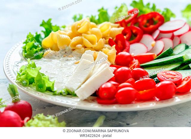 Dish with salad of fresh vegetables, pasta and artisan cheese on white table, selective focus