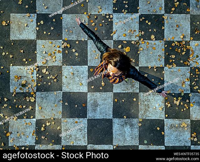 Carefree woman spinning on asphalt painted with checked pattern