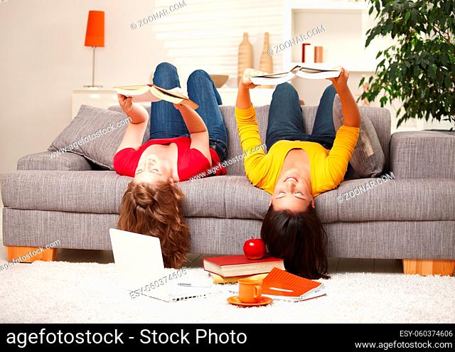Teenage girls sitting upside down on sofa reading books