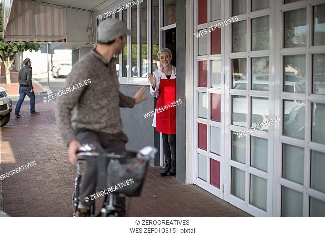 Shop assistant waving at man on bicycle outside shop