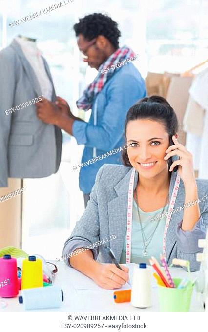Smiling fashion designer calling while her colleague adjusting blazer on a mannequin