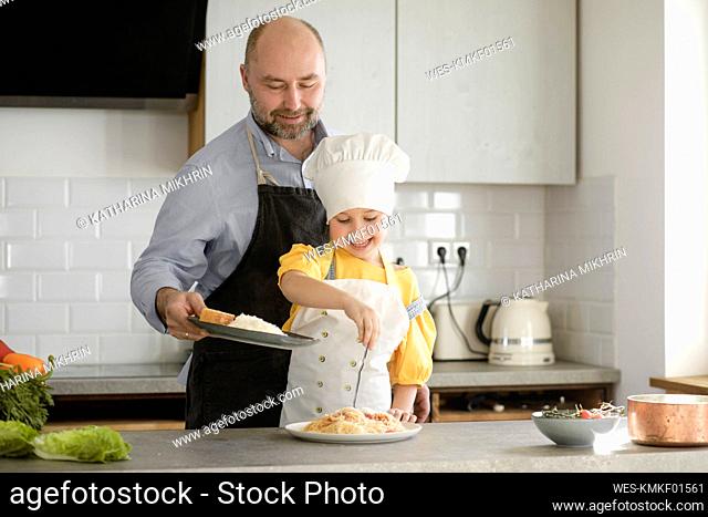 Smiling daughter putting seasoning in food while standing at kitchen