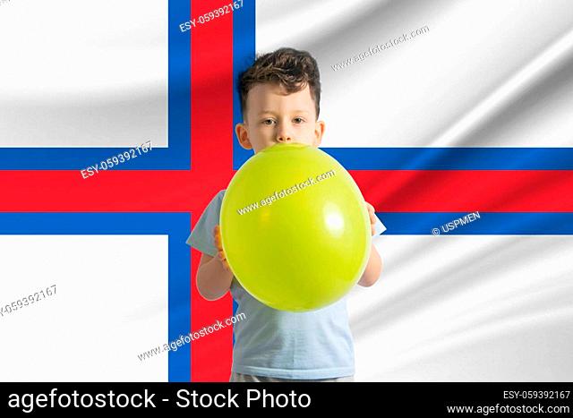 Children's day in Faroe Islands. White boy with a balloon on the background of the flag of Faroe Islands. Childrens day celebration concept