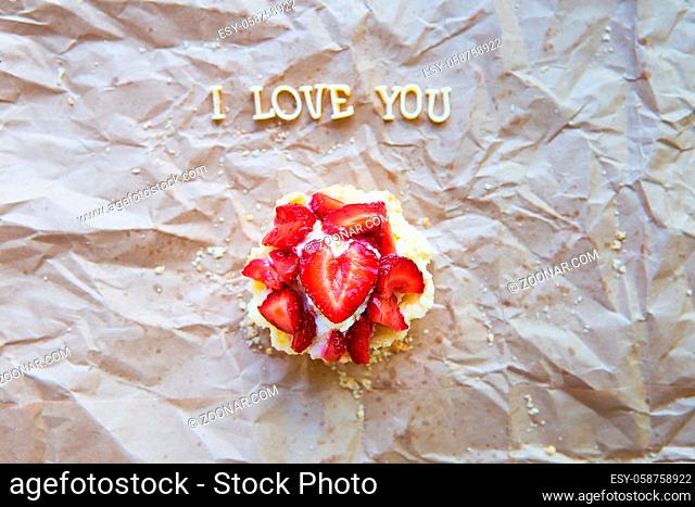Bright cupcake with strawberries lies on craft paper, the inscription I love you
