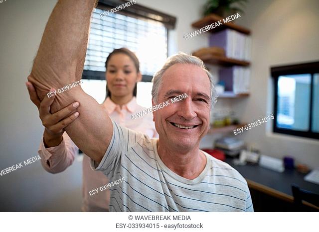 Smiling senior man looking away while female doctor examining elbow
