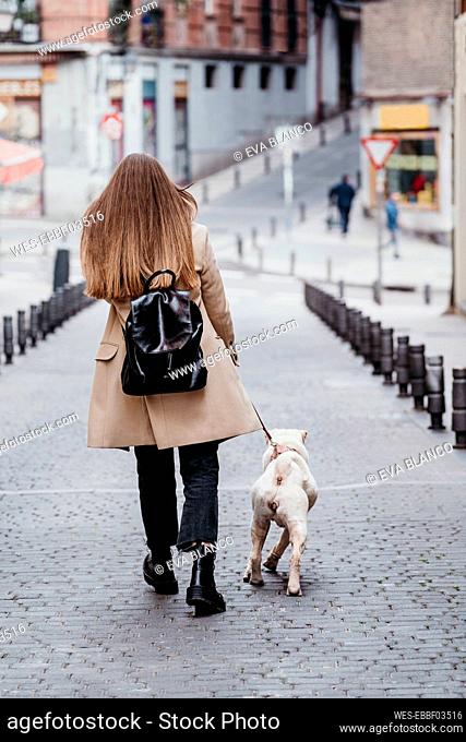 Brown hair woman walking with dog on footpath