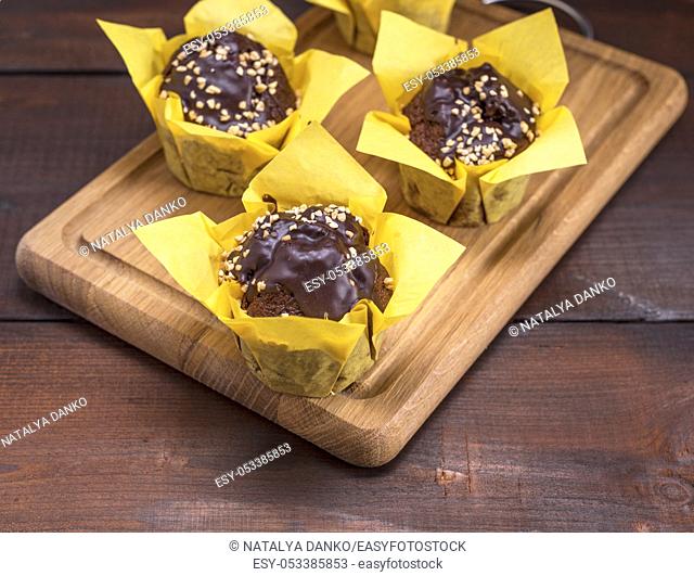 chocolate banana muffins sprinkled with walnut and wrapped in yellow paper on a wooden kitchen board
