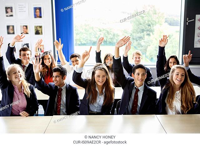Teenage schoolchildren with hands raised in classroom