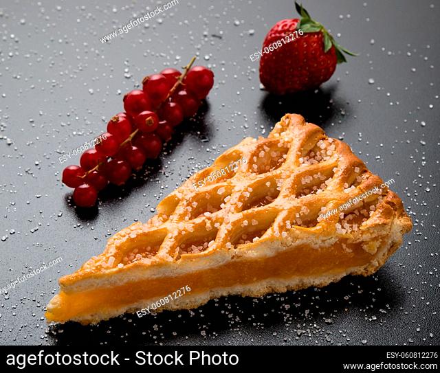 fresh apple pie slice on black table with currant and strawberry