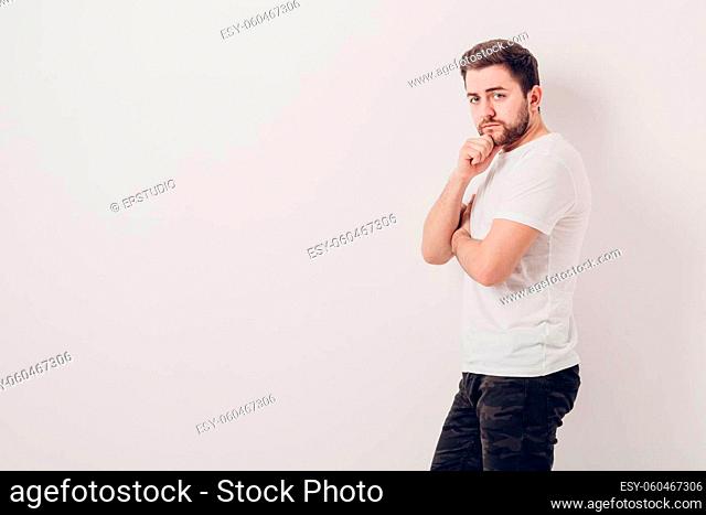portrait of handsome young thinking man with beard ooking at camera against white wall